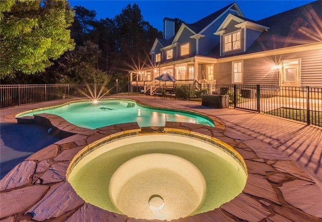 pool at twilight featuring a patio area and an in ground hot tub