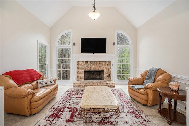 living room featuring light tile patterned floors, high vaulted ceiling, wainscoting, and a brick fireplace