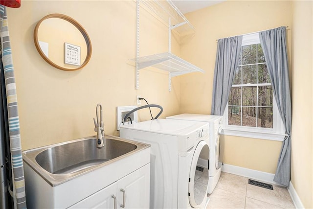 clothes washing area with visible vents, light tile patterned floors, a sink, cabinet space, and washing machine and clothes dryer
