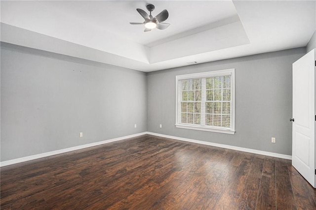 empty room with wood-type flooring, baseboards, a raised ceiling, and ceiling fan