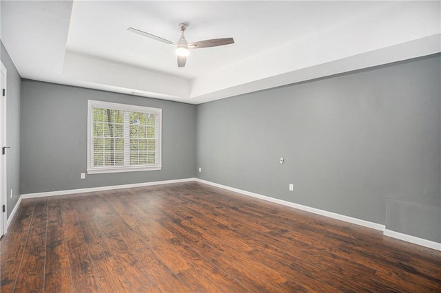 empty room with a tray ceiling, baseboards, a ceiling fan, and wood finished floors