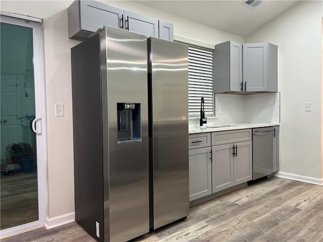 kitchen with appliances with stainless steel finishes, sink, gray cabinetry, and light hardwood / wood-style floors