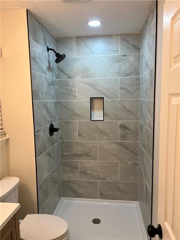 bathroom featuring vanity, toilet, a textured ceiling, and a tile shower