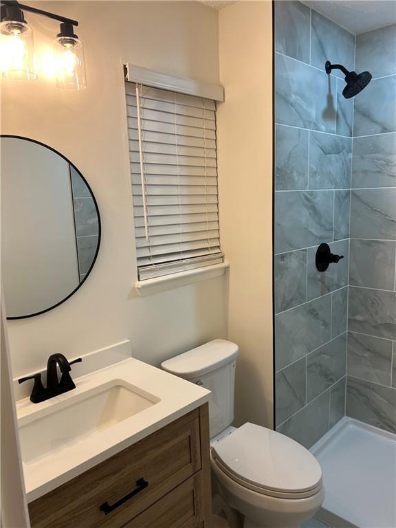 bathroom with vanity, toilet, and tiled shower