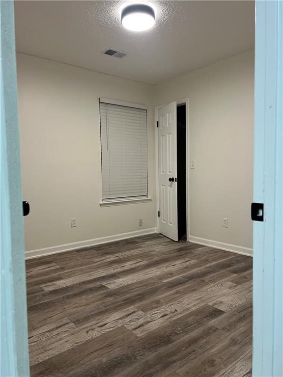 empty room with dark hardwood / wood-style flooring and a textured ceiling