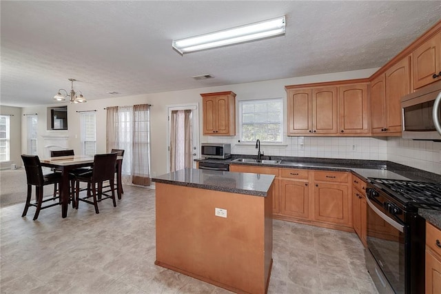 kitchen with sink, black range with gas cooktop, decorative backsplash, a kitchen island, and decorative light fixtures