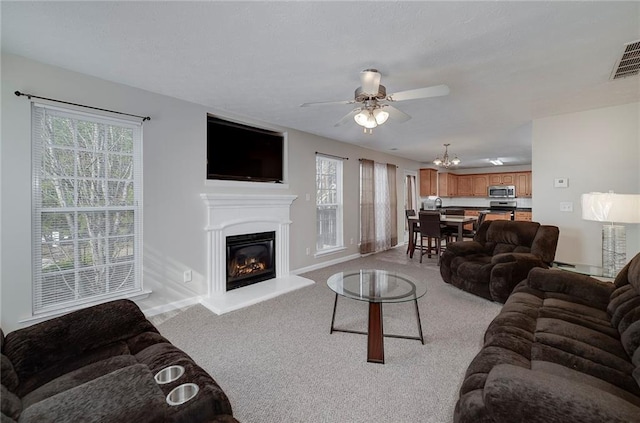 living room featuring a wealth of natural light, ceiling fan with notable chandelier, and light carpet