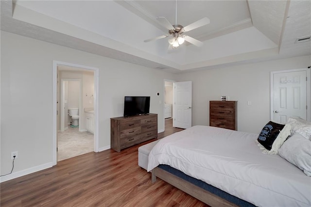 bedroom featuring hardwood / wood-style flooring, ceiling fan, ensuite bathroom, and a tray ceiling