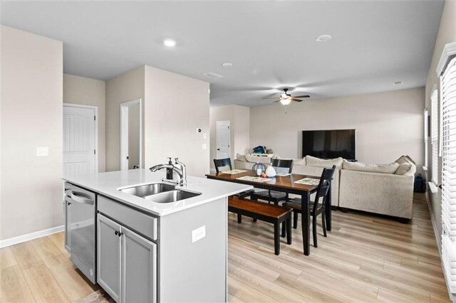 kitchen featuring gray cabinetry, sink, stainless steel dishwasher, light hardwood / wood-style floors, and a kitchen island with sink