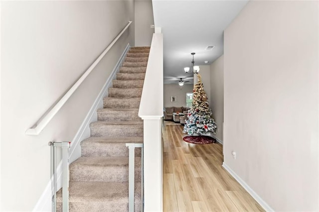 stairs featuring ceiling fan with notable chandelier and hardwood / wood-style flooring