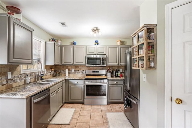 kitchen with appliances with stainless steel finishes, gray cabinetry, tasteful backsplash, and sink