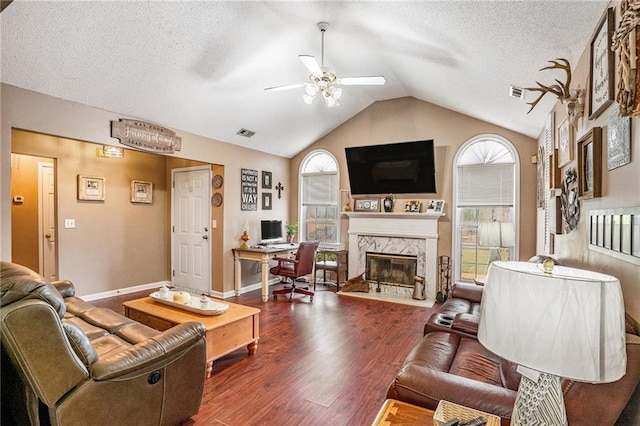 living room featuring a high end fireplace, lofted ceiling, dark wood-type flooring, ceiling fan, and a textured ceiling