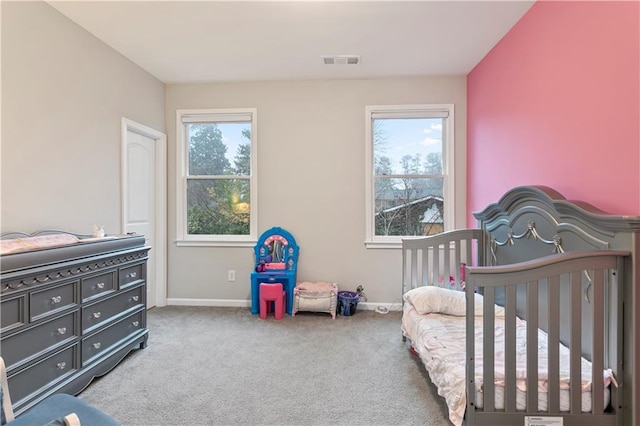 bedroom with a crib, light colored carpet, and multiple windows