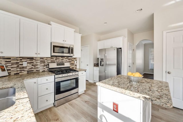 kitchen featuring a kitchen island, white cabinetry, decorative backsplash, light stone counters, and stainless steel appliances