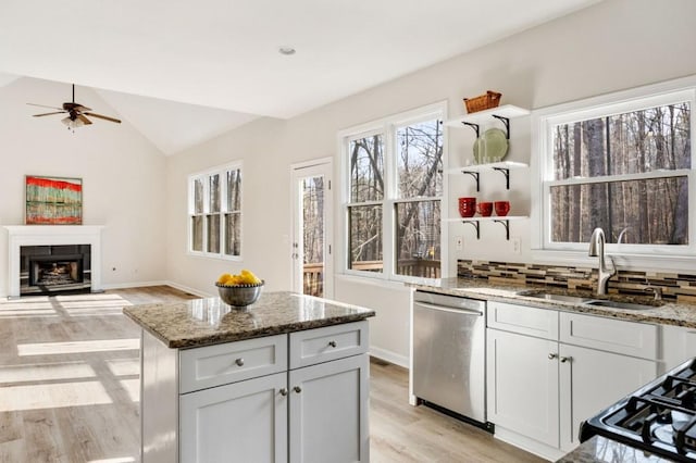 kitchen with lofted ceiling, sink, a center island, stainless steel dishwasher, and light stone counters