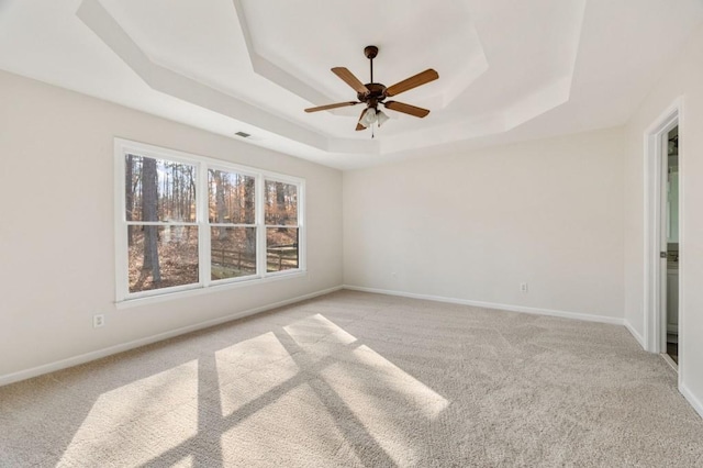 spare room with a raised ceiling, light colored carpet, and ceiling fan