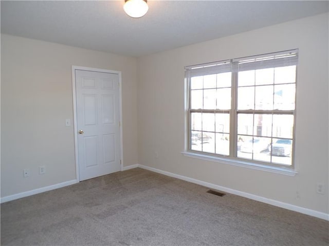 empty room with carpet, visible vents, and baseboards