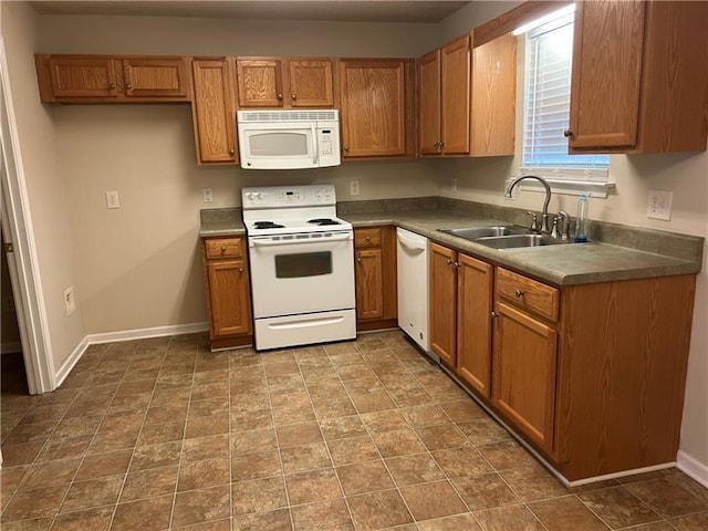 kitchen with brown cabinetry, white appliances, a sink, and baseboards