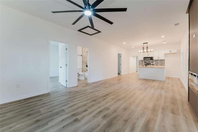 unfurnished living room with ceiling fan with notable chandelier and light wood-type flooring