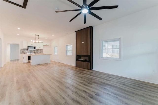 unfurnished living room featuring ceiling fan with notable chandelier, light hardwood / wood-style floors, and plenty of natural light