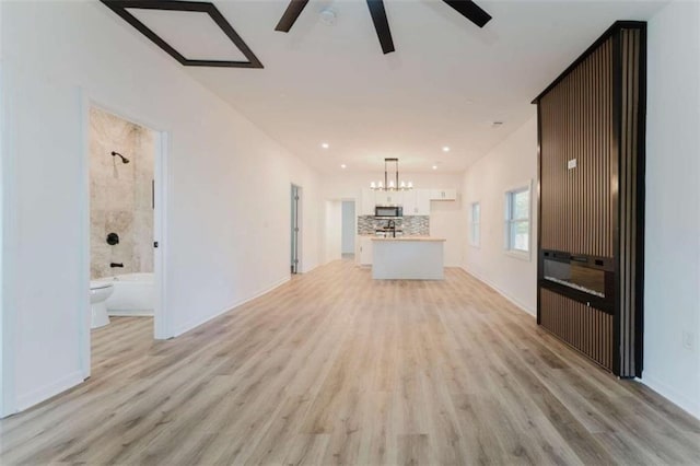 unfurnished living room with ceiling fan with notable chandelier and light hardwood / wood-style floors