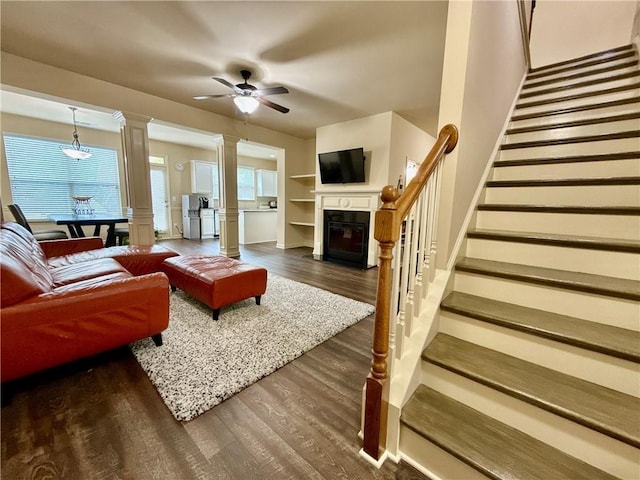 2351 Attewood Dr, Buford, GA 30519 - living room with stairway, dark wood-style floors, a ceiling fan, a glass covered fireplace, and decorative columns