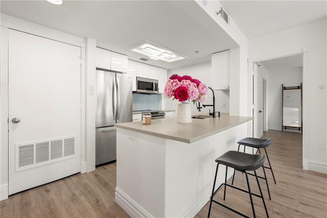 1280 W Peachtree St NW Unit 2409, Atlanta, GA 30309 - kitchen with appliances with stainless steel finishes, white cabinetry, a kitchen bar, light wood-type flooring, and backsplash