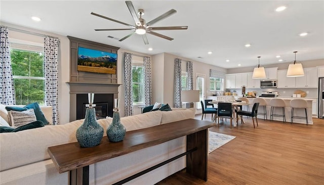 living room featuring light wood finished floors, a ceiling fan, a glass covered fireplace, and recessed lighting