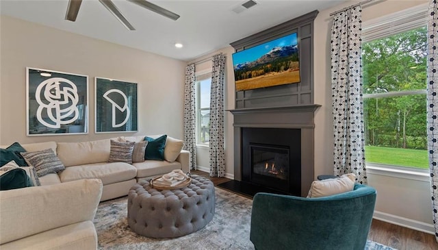 living room featuring baseboards, a ceiling fan, wood finished floors, a glass covered fireplace, and healthy amount of natural light