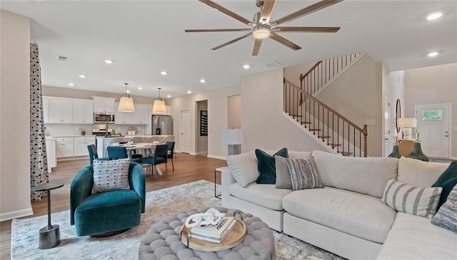 living room with light wood-style floors, a ceiling fan, stairs, baseboards, and recessed lighting