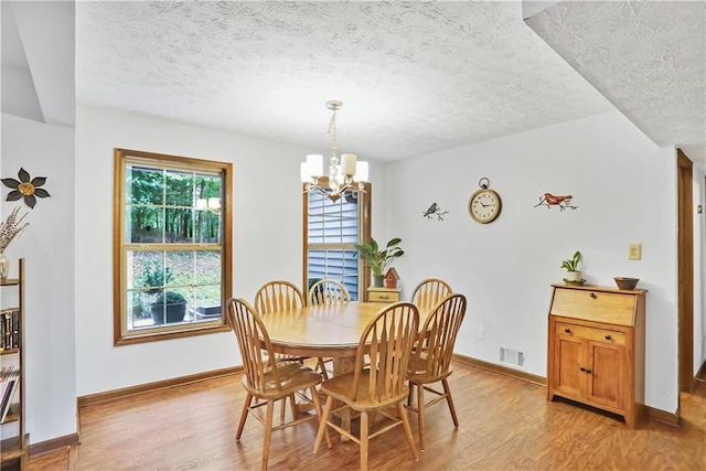 dining room with a chandelier, visible vents, light wood-style flooring, and a textured ceiling