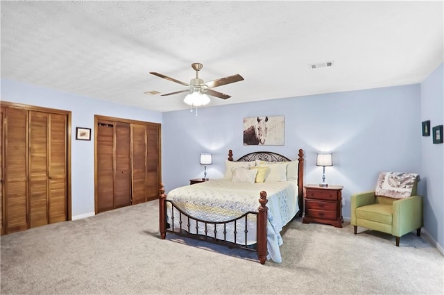 carpeted bedroom featuring baseboards, visible vents, ceiling fan, a textured ceiling, and multiple closets