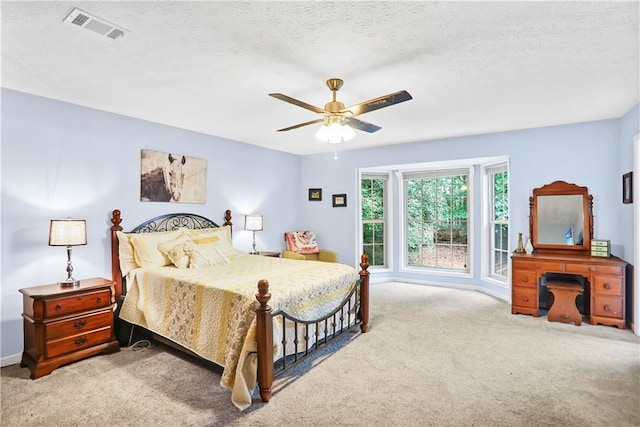 bedroom featuring light colored carpet, visible vents, ceiling fan, and a textured ceiling