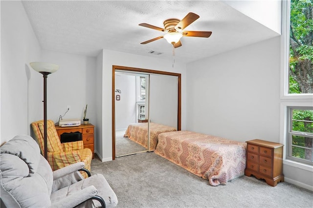 bedroom with a textured ceiling, light colored carpet, a ceiling fan, visible vents, and a closet