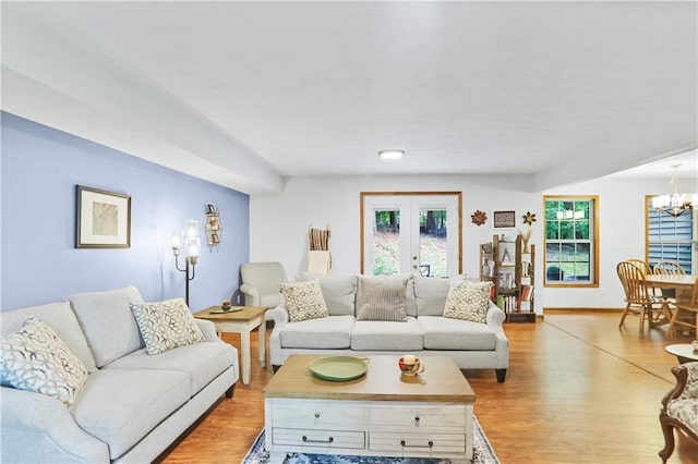 living area with a notable chandelier, french doors, a wealth of natural light, and light wood-style floors