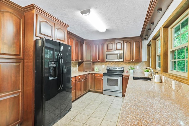 kitchen with light tile patterned floors, stainless steel appliances, a sink, light stone countertops, and tasteful backsplash