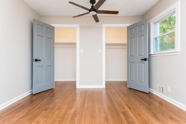 unfurnished bedroom with a walk in closet, a closet, light hardwood / wood-style flooring, and ceiling fan