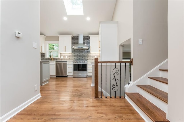 kitchen featuring sink, wall chimney exhaust hood, appliances with stainless steel finishes, white cabinets, and light wood-type flooring