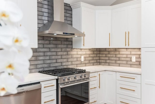 kitchen with decorative backsplash, appliances with stainless steel finishes, white cabinetry, and wall chimney range hood