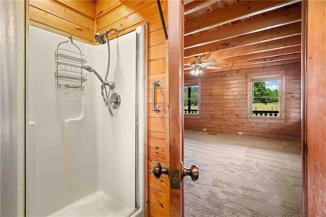bathroom with beamed ceiling, wood walls, a shower stall, and a healthy amount of sunlight