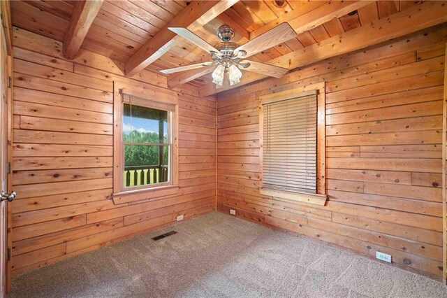 carpeted empty room featuring wooden walls, beam ceiling, a ceiling fan, wooden ceiling, and visible vents