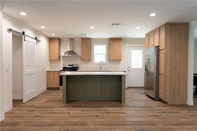 kitchen featuring a barn door, light countertops, wall chimney exhaust hood, stainless steel appliances, and wood finished floors