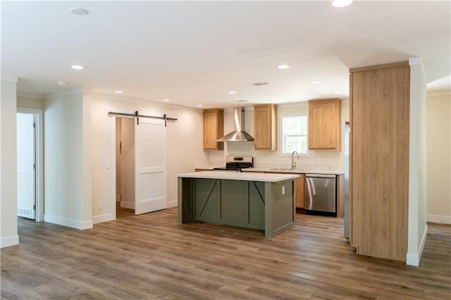 kitchen with wall chimney range hood, a kitchen island, appliances with stainless steel finishes, a barn door, and a sink
