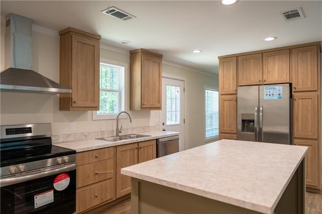 kitchen featuring visible vents, crown molding, wall chimney range hood, a sink, and appliances with stainless steel finishes