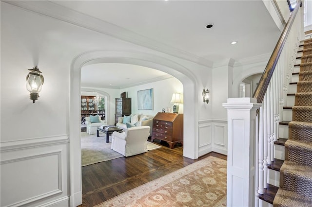 entrance foyer featuring a wainscoted wall, ornamental molding, wood finished floors, arched walkways, and a decorative wall