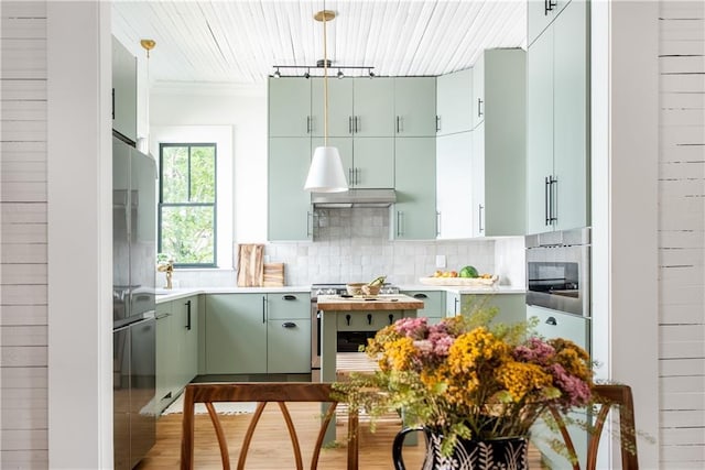 kitchen with under cabinet range hood, decorative backsplash, green cabinetry, and freestanding refrigerator