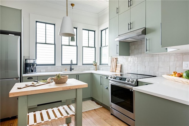 kitchen with under cabinet range hood, stainless steel appliances, a sink, green cabinets, and ornamental molding