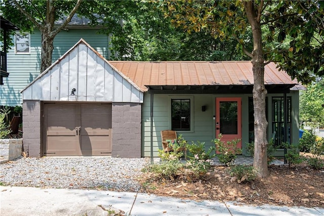 view of front facade with driveway, a garage, concrete block siding, and metal roof