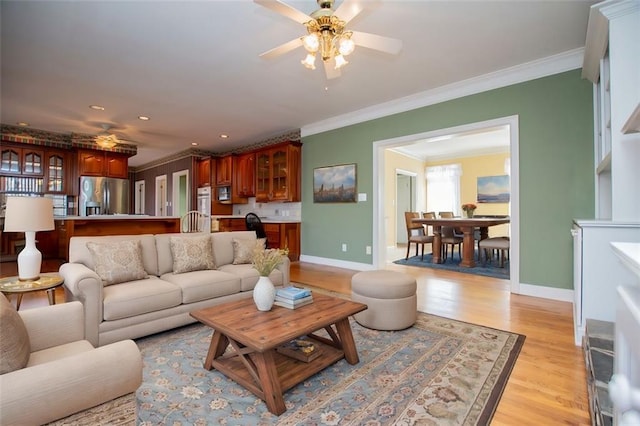 living room featuring baseboards, light wood finished floors, a ceiling fan, and crown molding