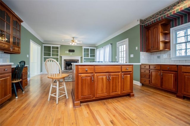 kitchen with light wood finished floors, glass insert cabinets, ornamental molding, a stone fireplace, and a kitchen bar